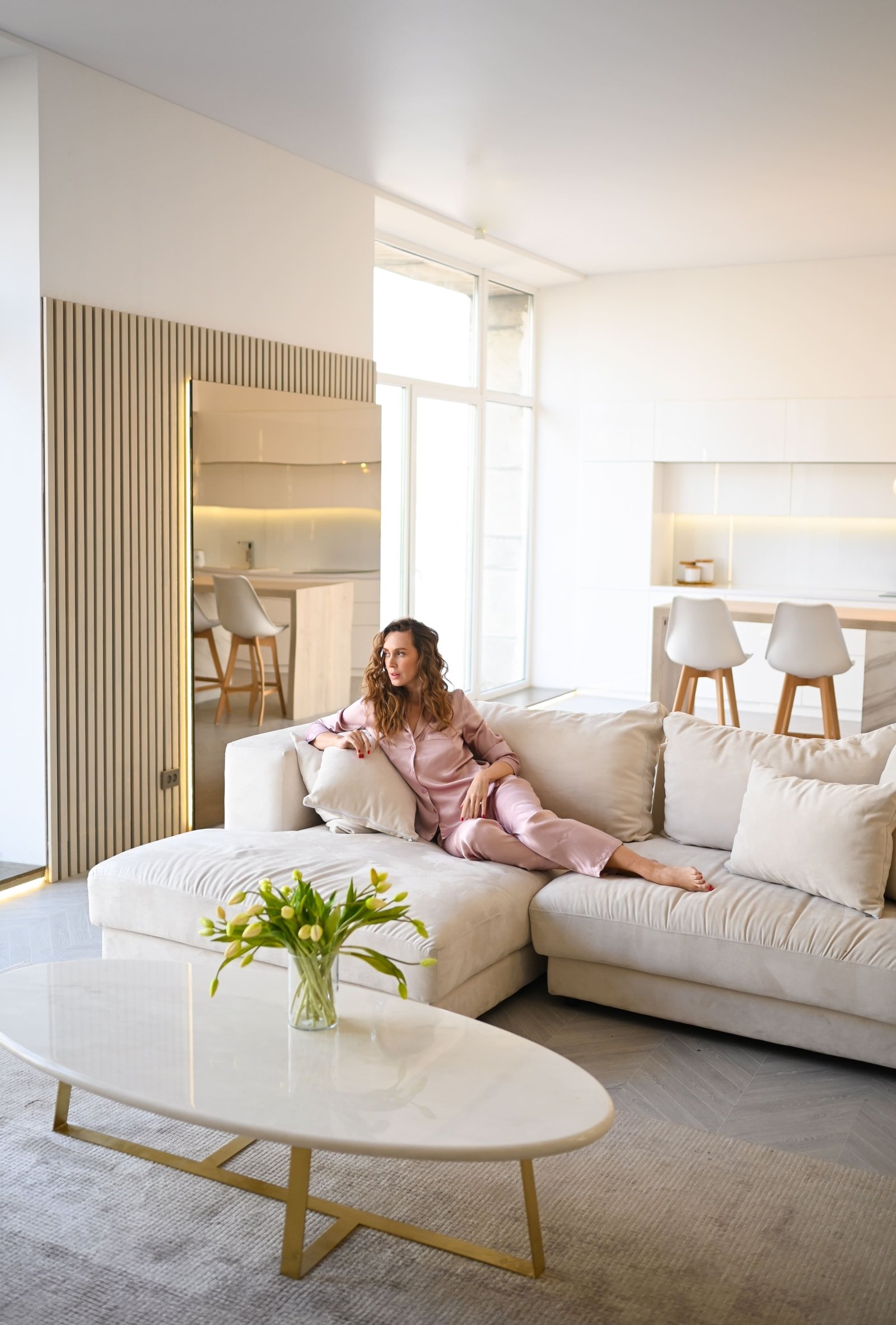 beautiful-young-woman-with-curly-hair-pink-pajamas-lying-white-couch-sofa-morning-scandinavian-style-living-room-kitchen-interior