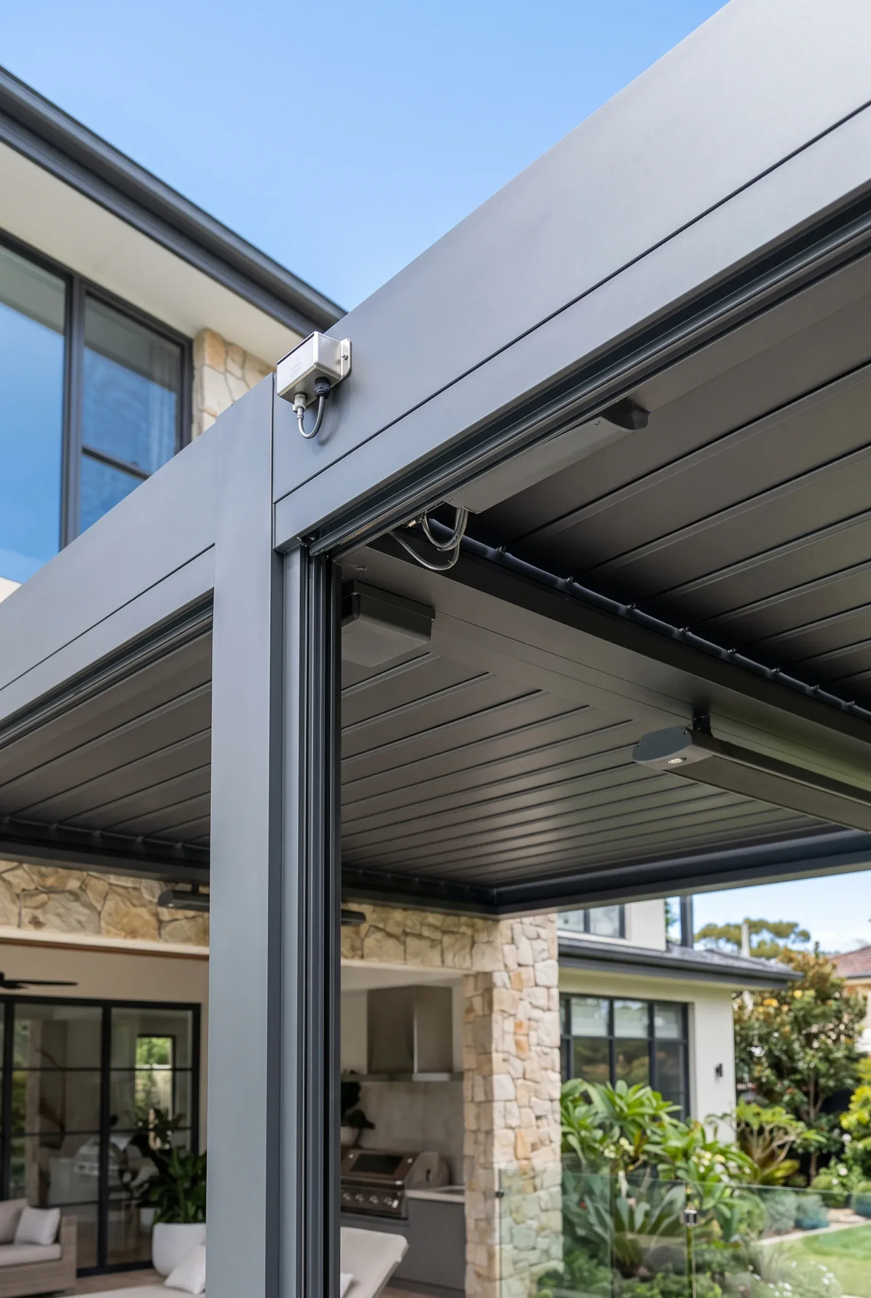 Pérgola moderna de lamas gris oscuro con calentadores integrados, iluminación exterior y sensores climáticos en patio, diseño de exteriores de RBA Residences en Zapopan.