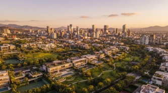 Vista aérea amplia de una comunidad residencial de lujo con villas modernas junto a espacios verdes exuberantes y vista al horizonte de la ciudad al atardecer, desarrollos exclusivos de RBA Residences en Zapopan.