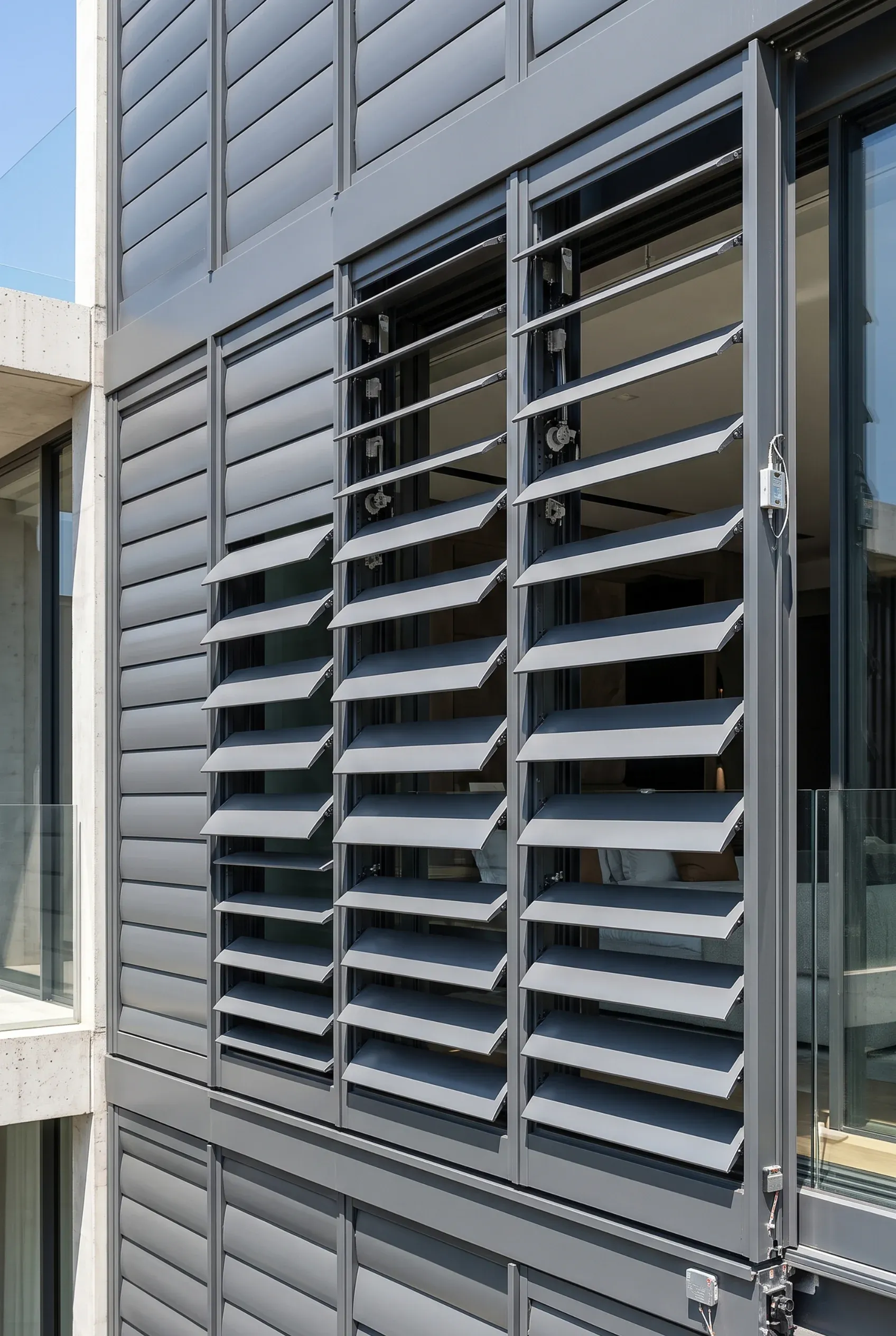 Fachada exterior con persianas abatibles motorizadas de aluminio gris oscuro ajustables sobre grandes ventanales, tecnología de control solar de RBA Residences en Zapopan.