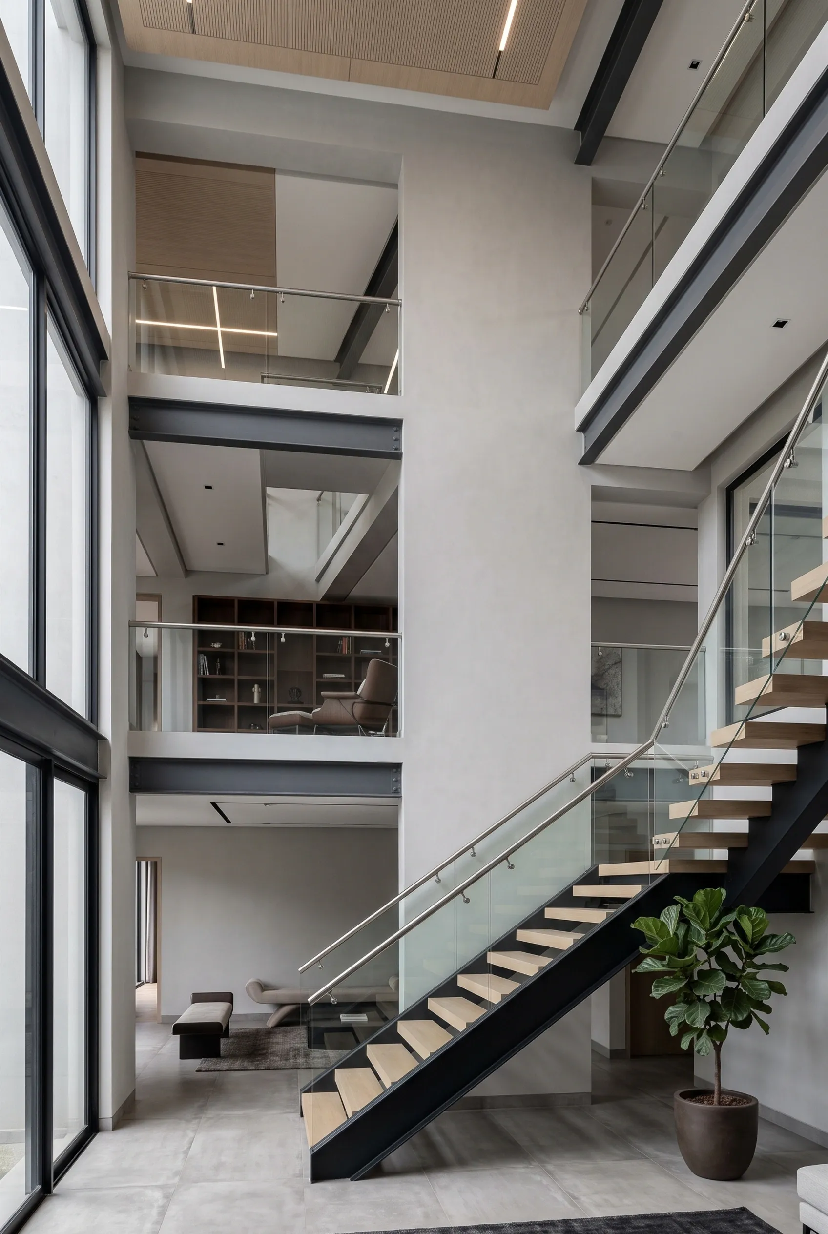 Atrio moderno de m&uacute;ltiples niveles con escaleras flotantes con barandales de vidrio, vigas estructurales de acero expuestas y ventanales de vidrio de piso a techo de varios pisos, conexi&oacute;n vertical de RBA Residences en Zapopan.