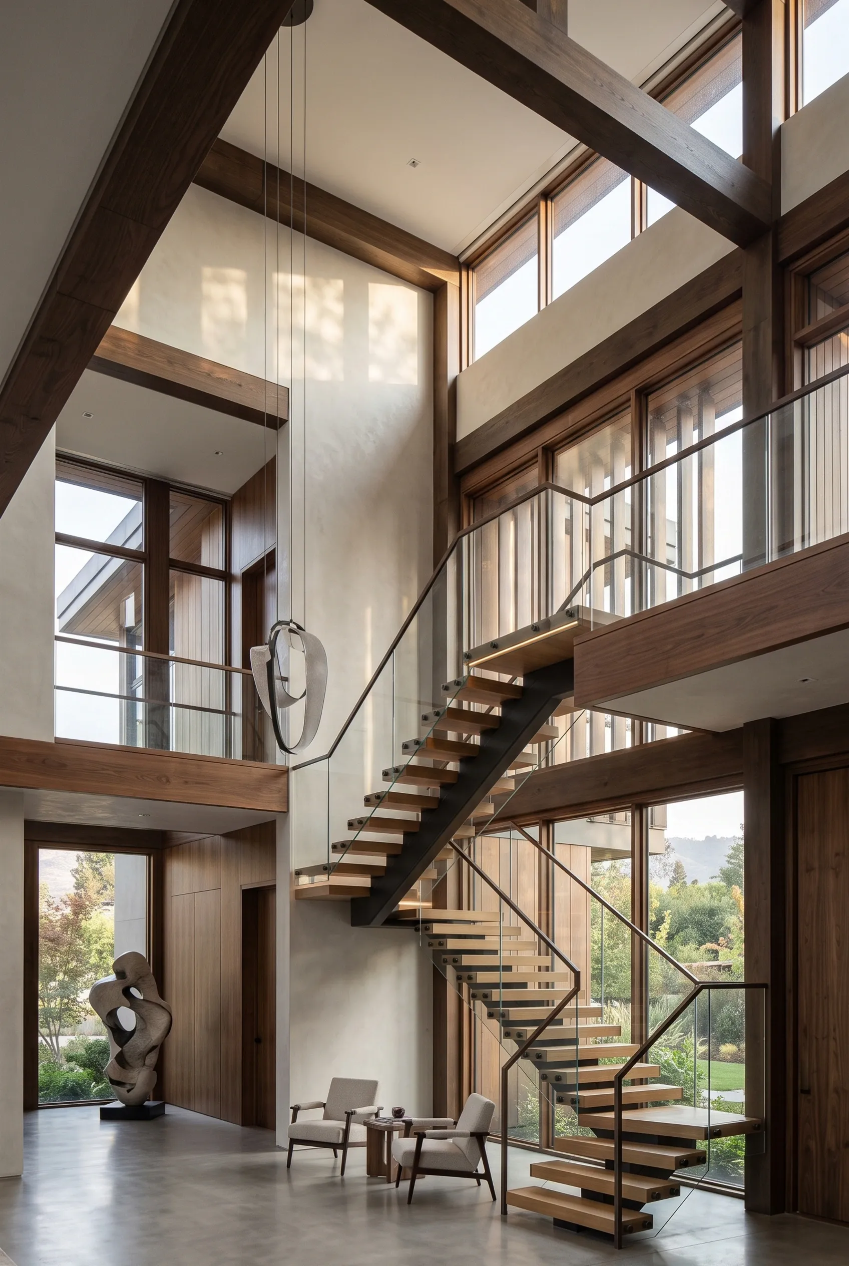 Vestíbulo moderno de doble altura con escaleras flotantes de madera y barandales de vidrio, vigas de madera oscura expuestas y ventanales de piso a techo, grandeza arquitectónica de RBA Residences en Zapopan.