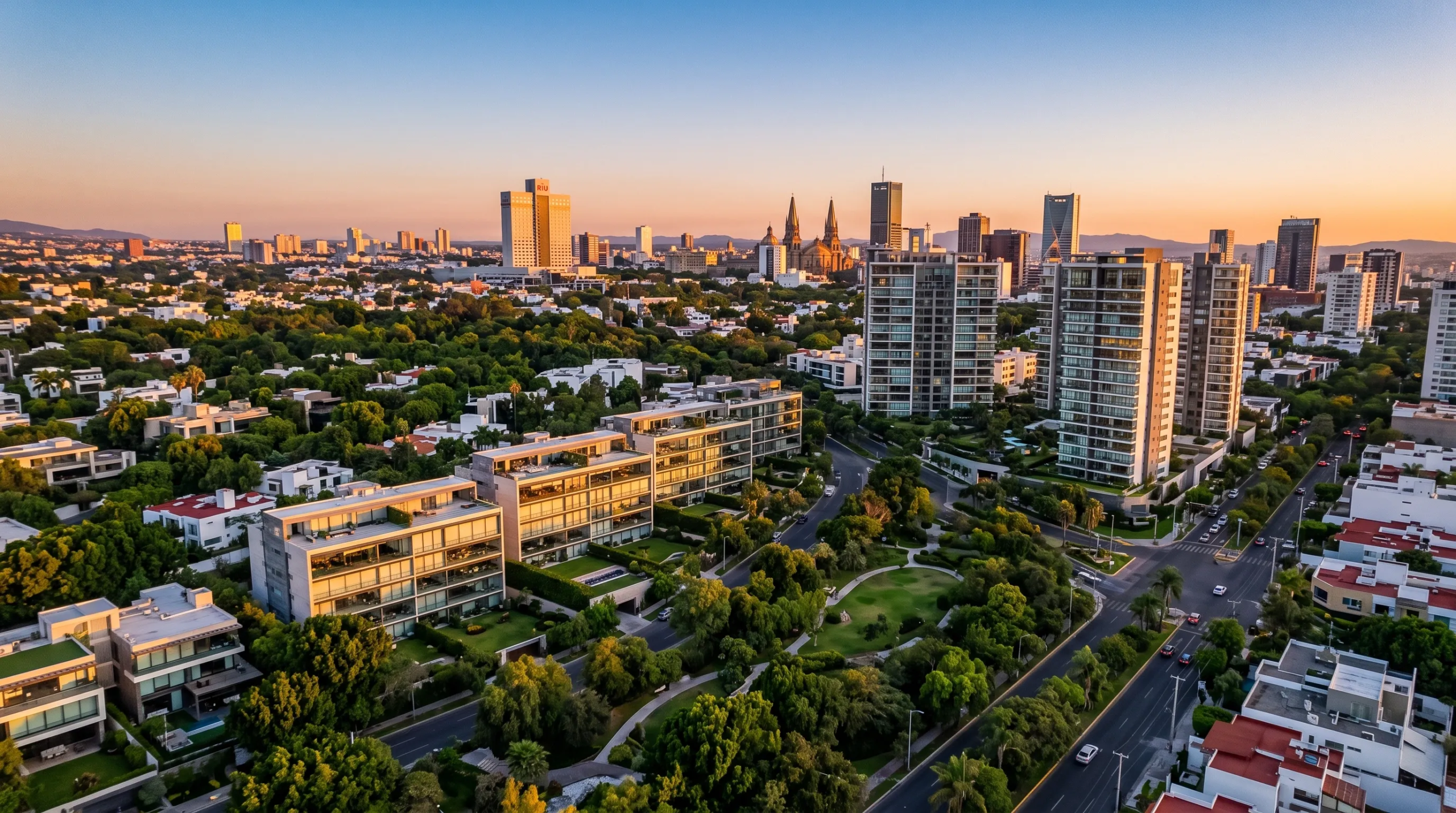 Vista aérea con dron de un distrito urbano de lujo de alta densidad con condominios de vidrio de altura media, corredores de parques exuberantes y horizonte urbano de rascacielos al atardecer dorado, vida vertical de RBA Residences en Zapopan.