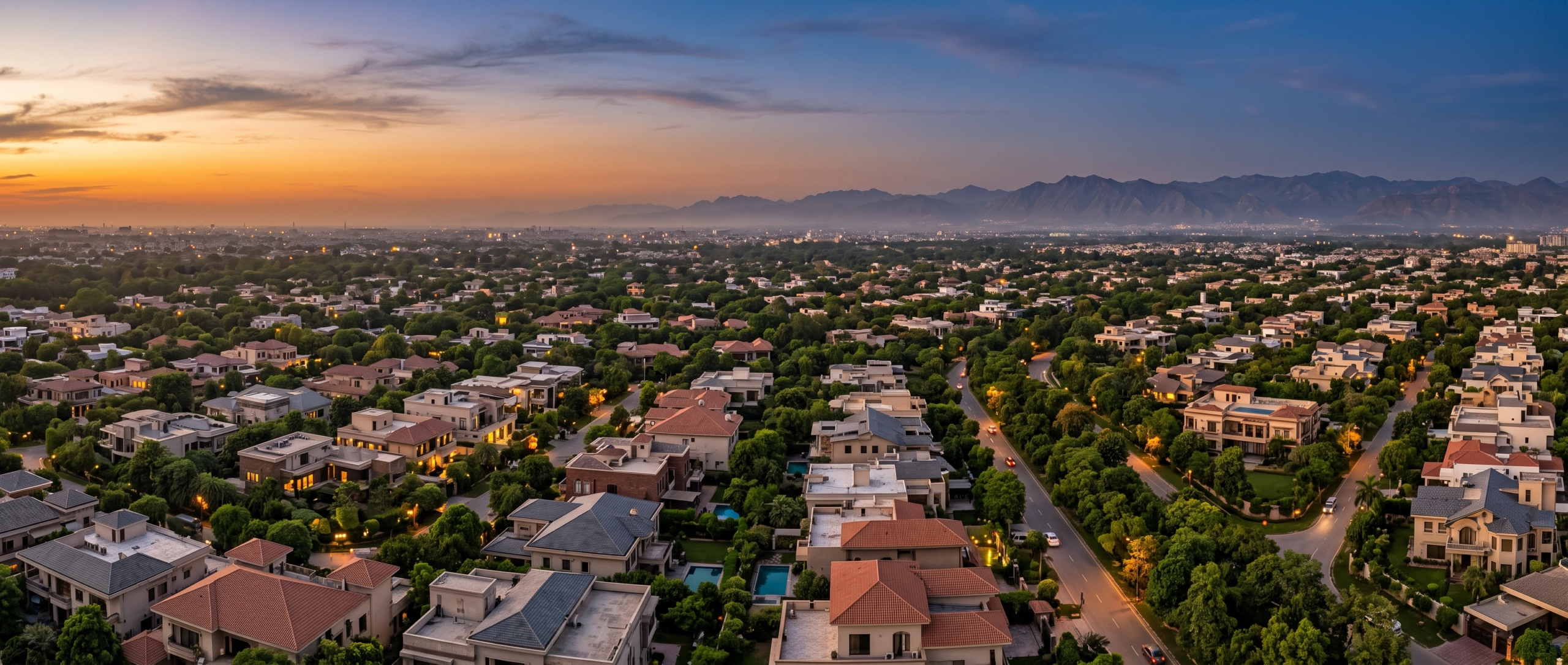 Fotografía aérea panorámica de una exclusiva comunidad residencial de lujo frente a una cadena montañosa al atardecer, con residencias modernas, doseles de árboles frondosos y calles sinuosas iluminadas, entorno montañoso de RBA Residences en Zapopan.